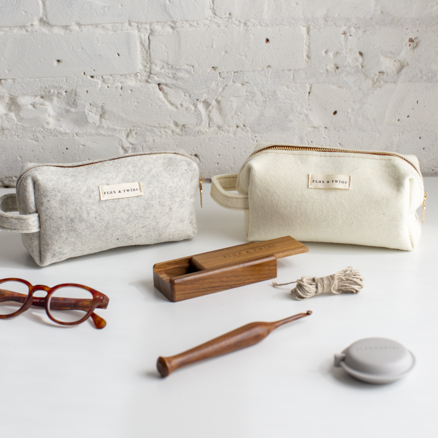 Two Flax & Twine Notions Bags with a wooden tool and eyeglasses on a light surface.