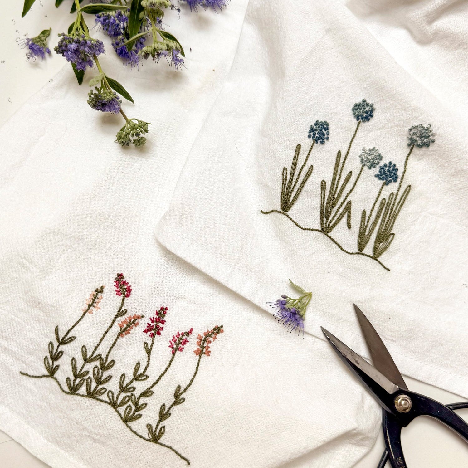 White towels with embroidered floral designs and a pair of scissors on a white background