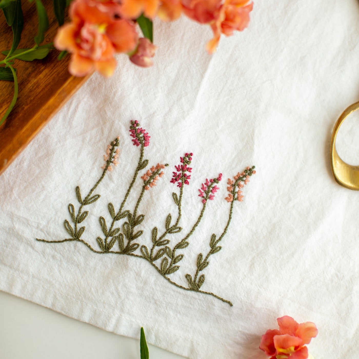 Embroidered floral design on a white fabric with orange flowers and green leaves.