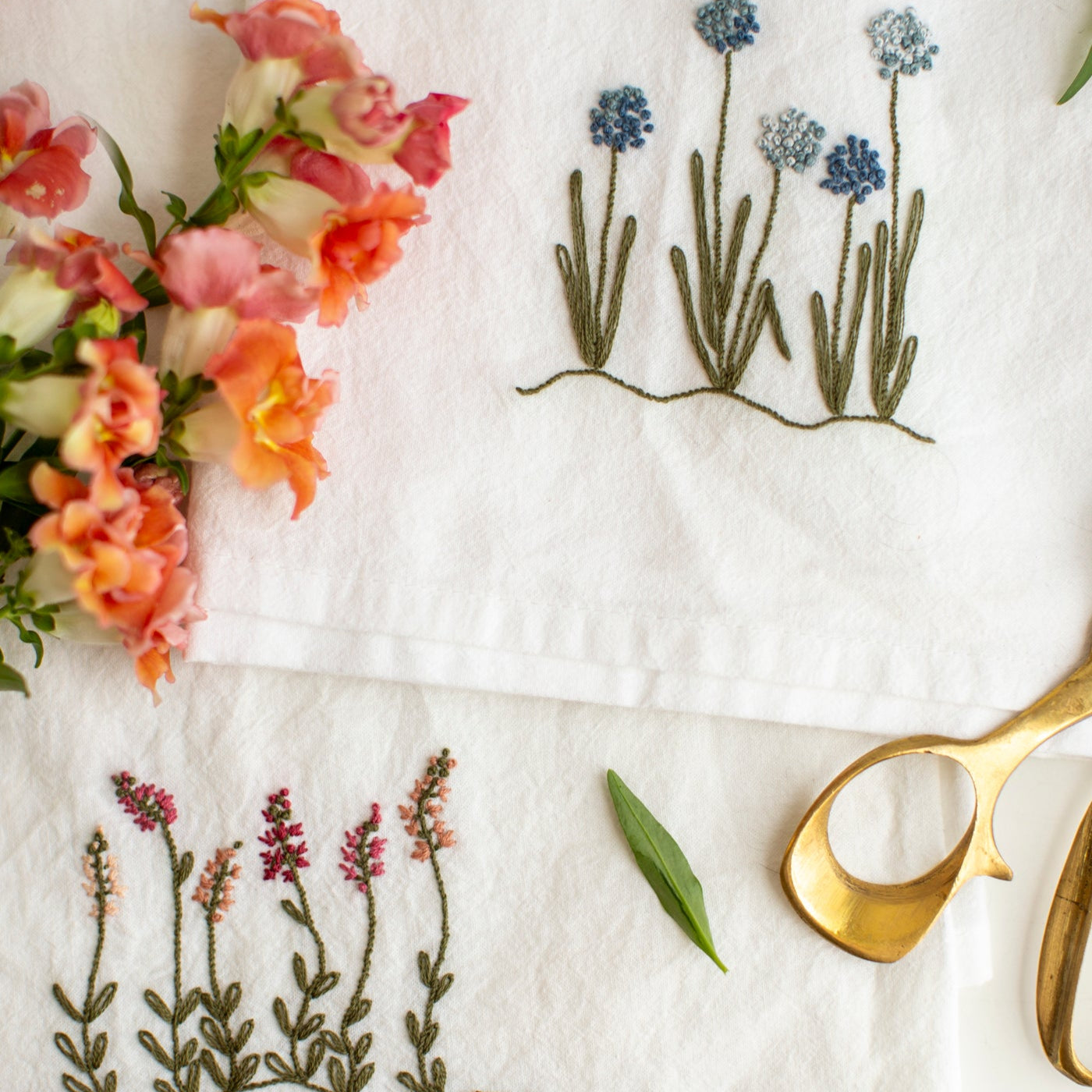 Embroidered flowers and plants on a white fabric with gold scissors and flowers.