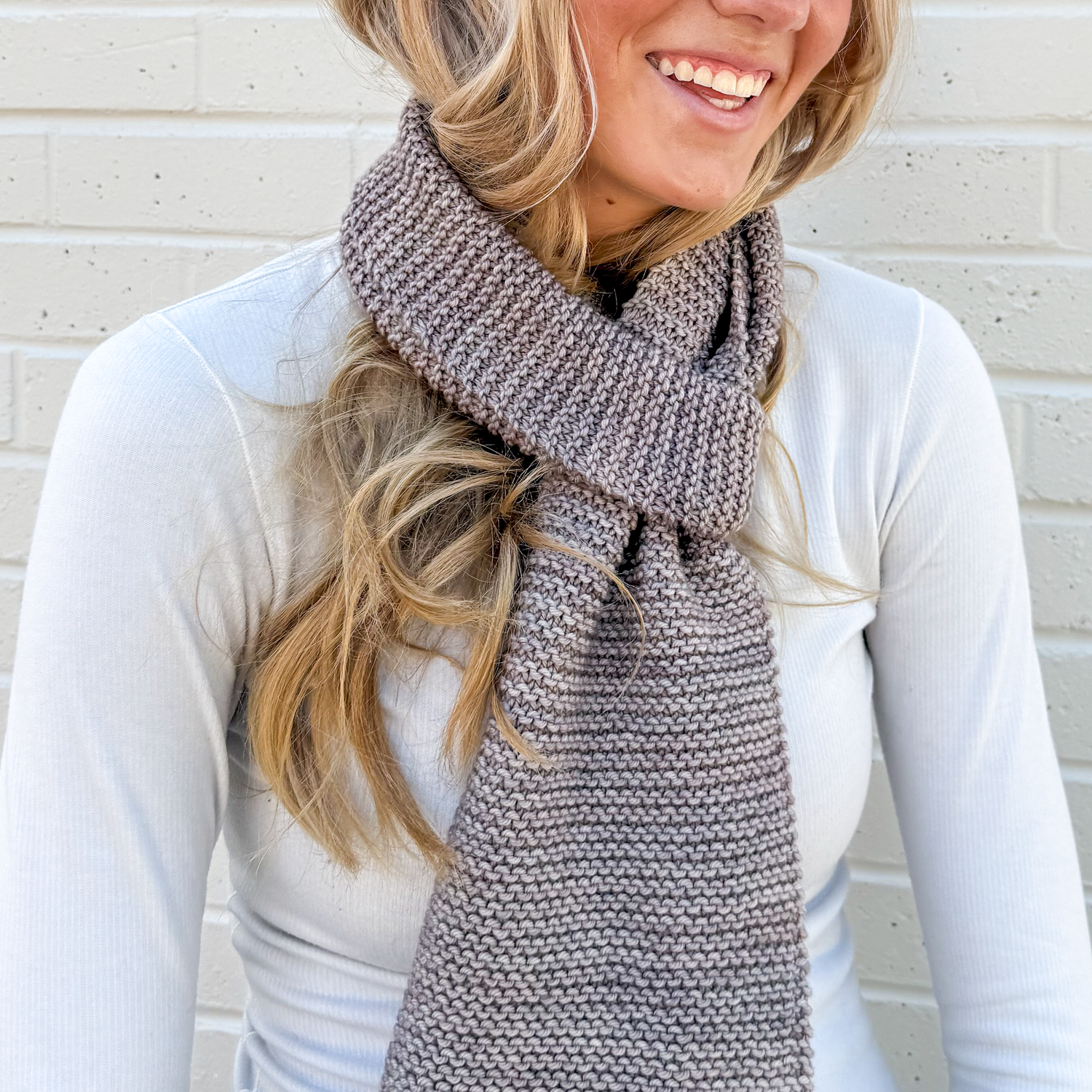Woman wearing a learn how to knit scarf against a light brick wall