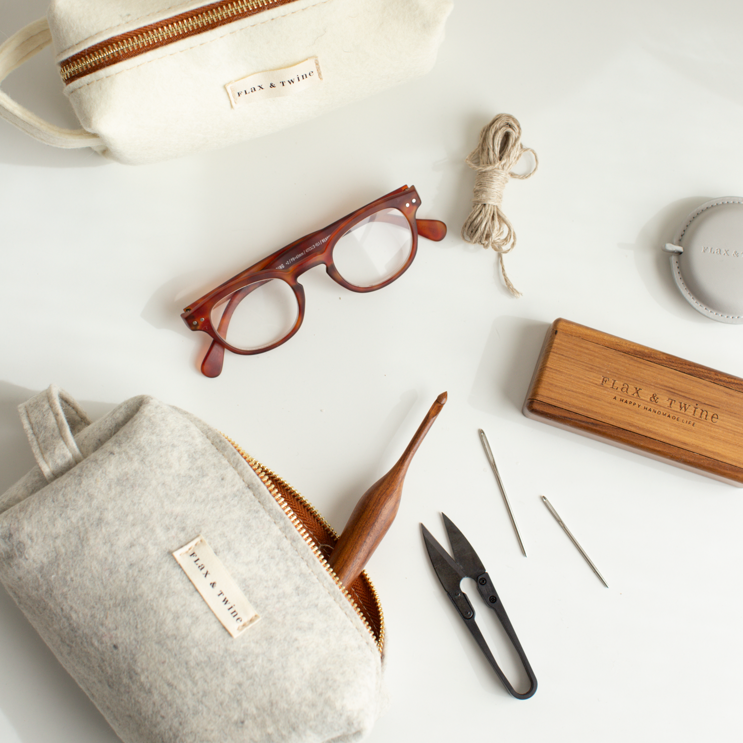 Various items including an off white notions bag, wooden sunglasses, gray notions bag, and small tools on a light surface.